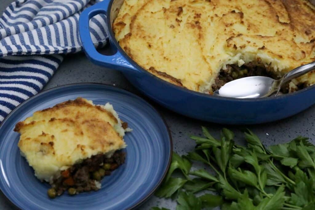 Shepherd's pie on a blue plate next to a casserole dish of the remaining shepherd's pie