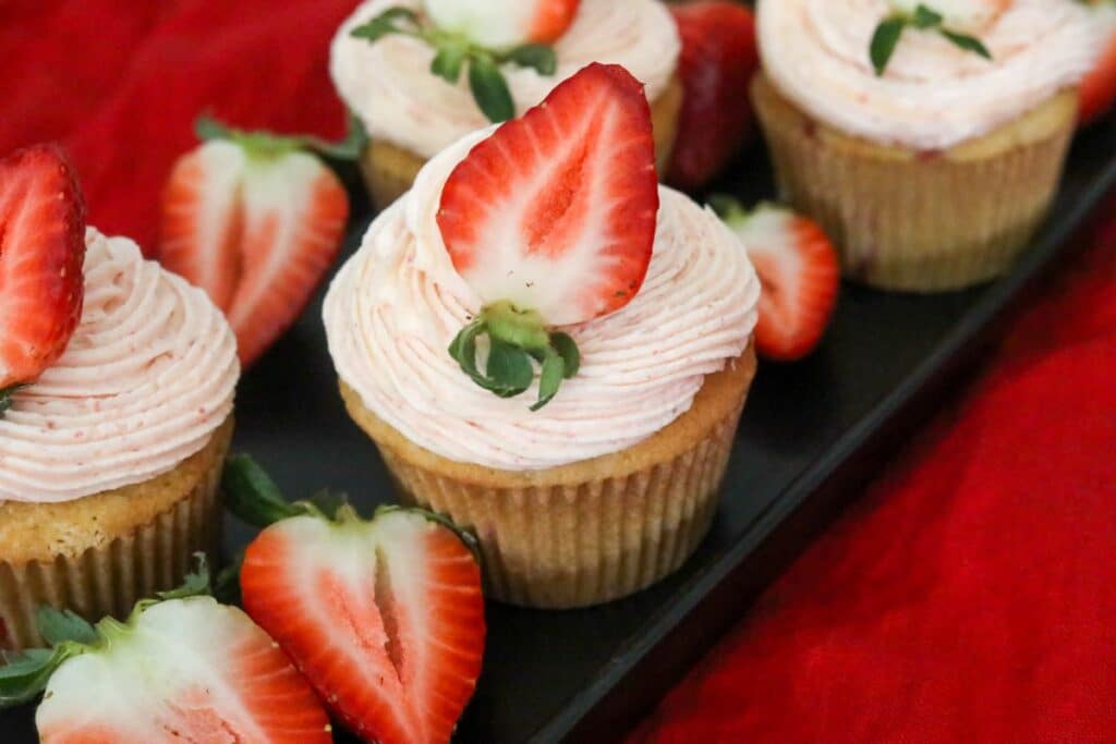 A black platter with strawberry cupcakes