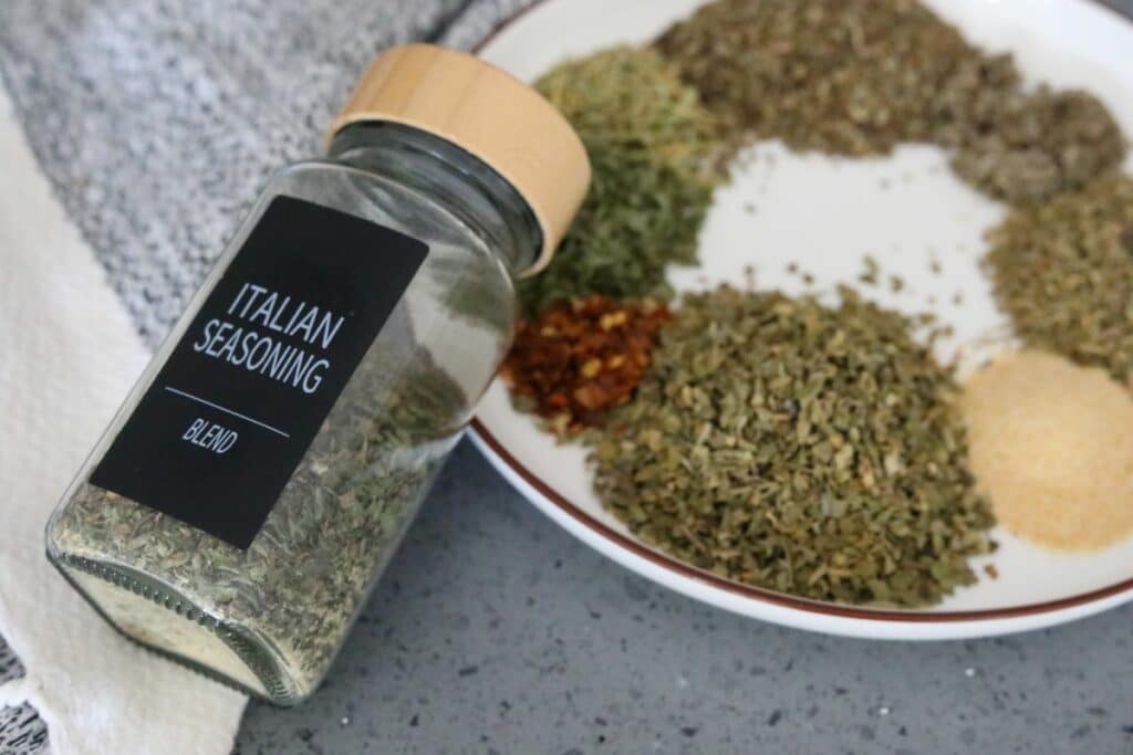 Ingredients of Italian seasoning on a plate with a labeled spice jar
