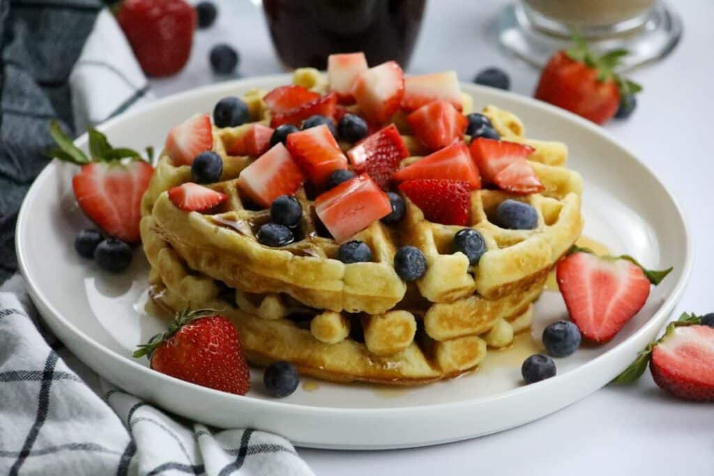 A white plate with 3 Belgian waffles topped with fresh fruit